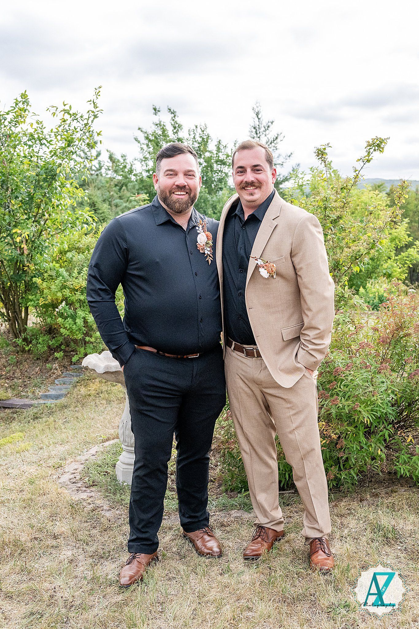 Two wedding attendees in contrasting black and tan suits posing outdoors.