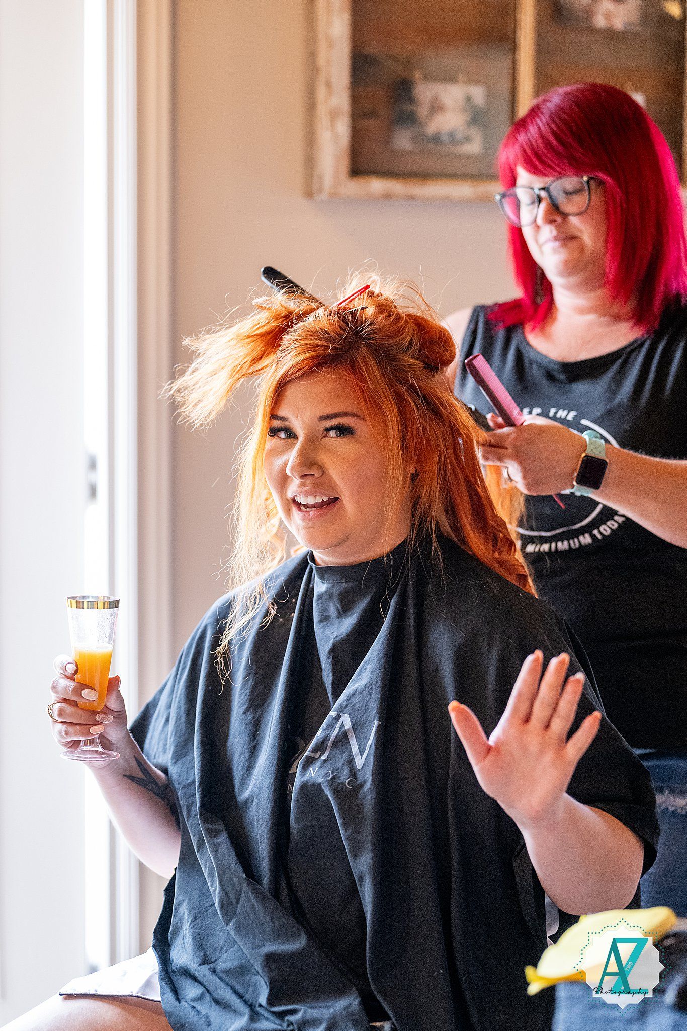 Person smiling while getting their hair styled at a salon in a black salon cape.
