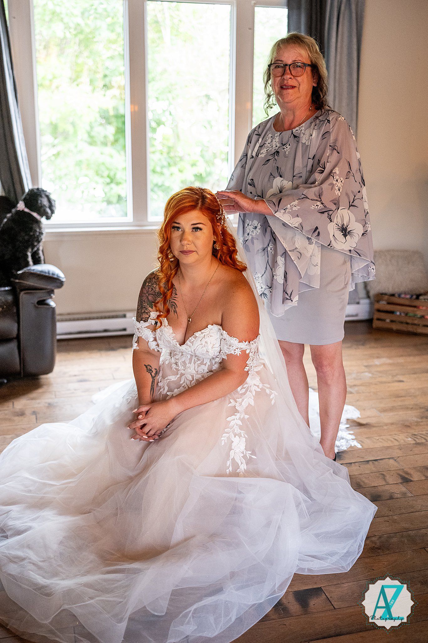 A bride sits gracefully in her white tulle wedding gown while getting ready in a sunlit room.