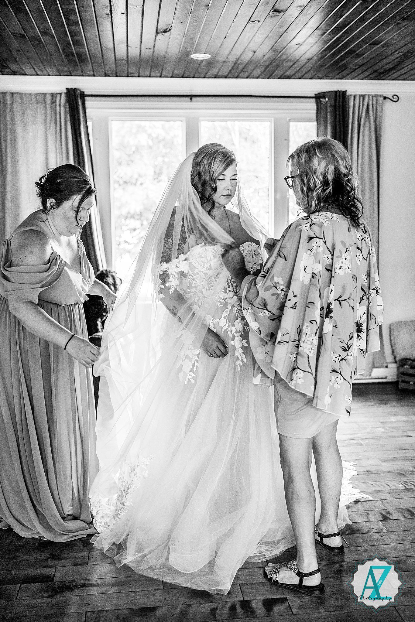 Black and white wedding photo series showing bridesmaids in matching dresses helping with the bride's gown.
