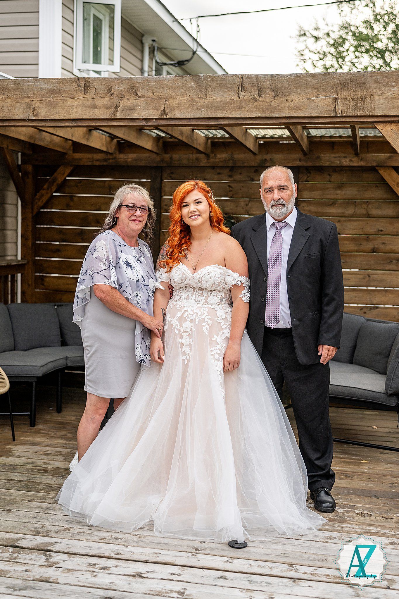 Wedding party poses on wooden patio with rustic decor and grey siding backdrop.