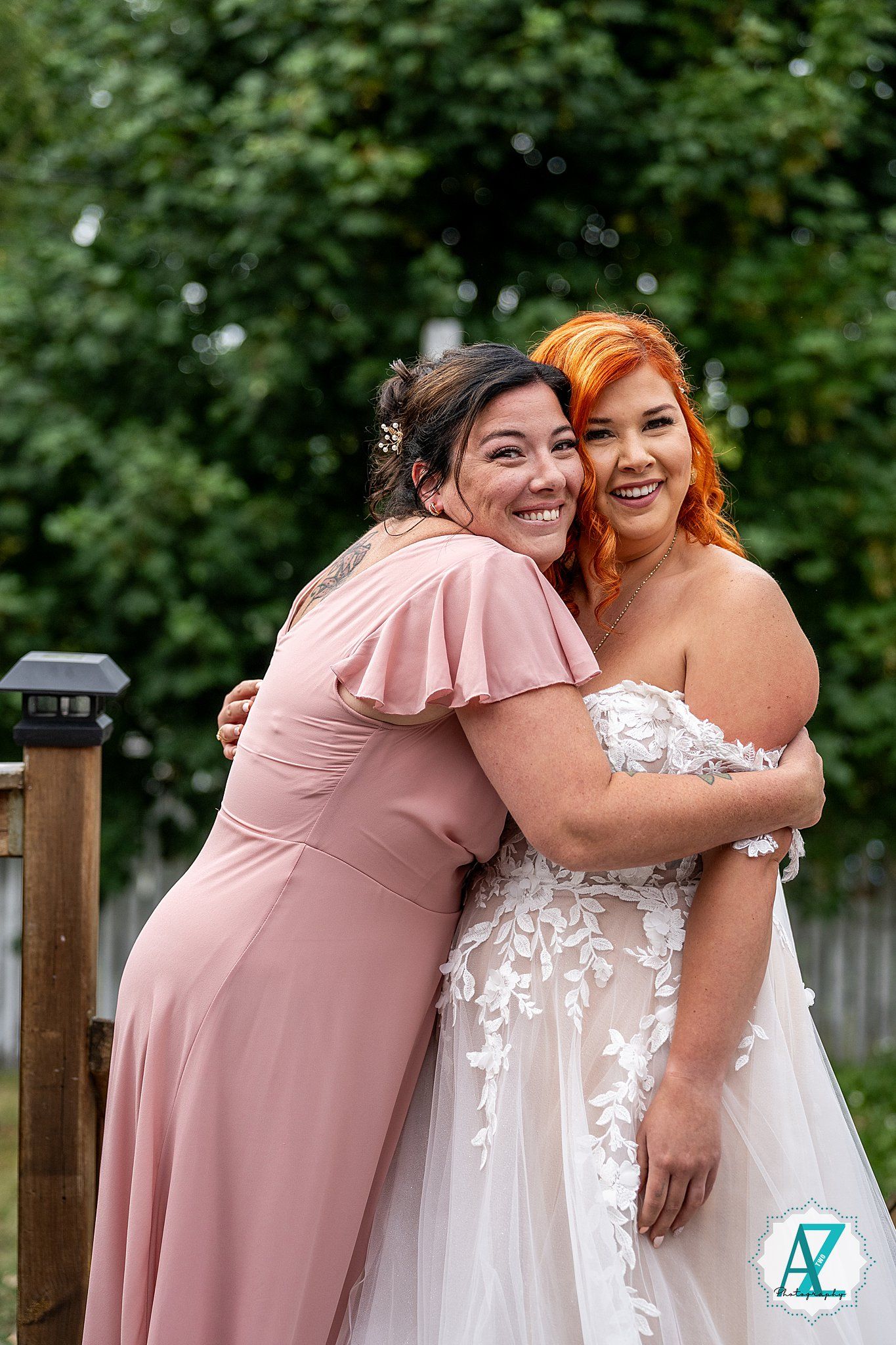 Two people share a joyful embrace at an outdoor wedding, one wearing a blush dress and one in white lace gown.