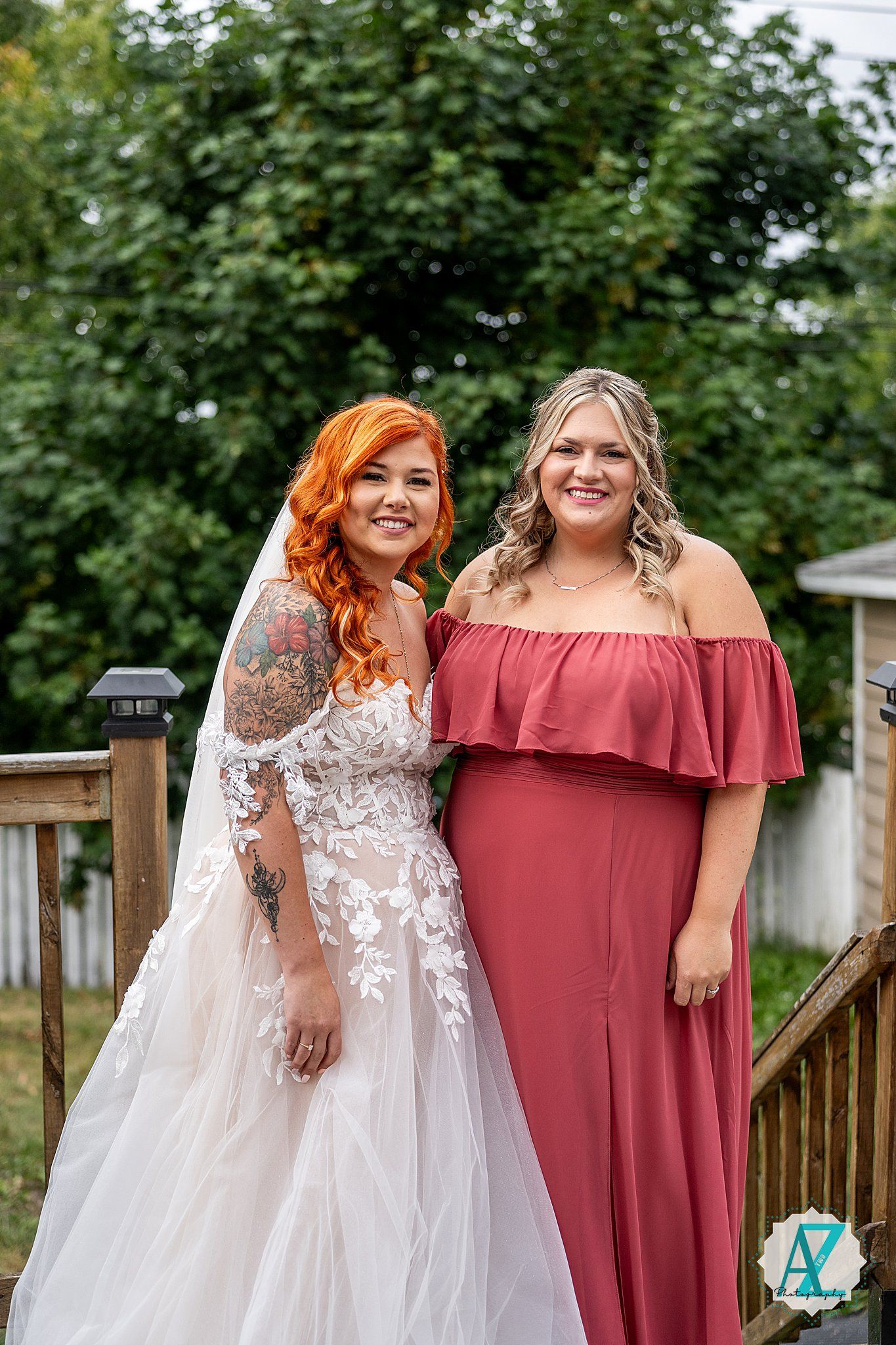 Wedding party members in burgundy and white pose together on wooden deck.