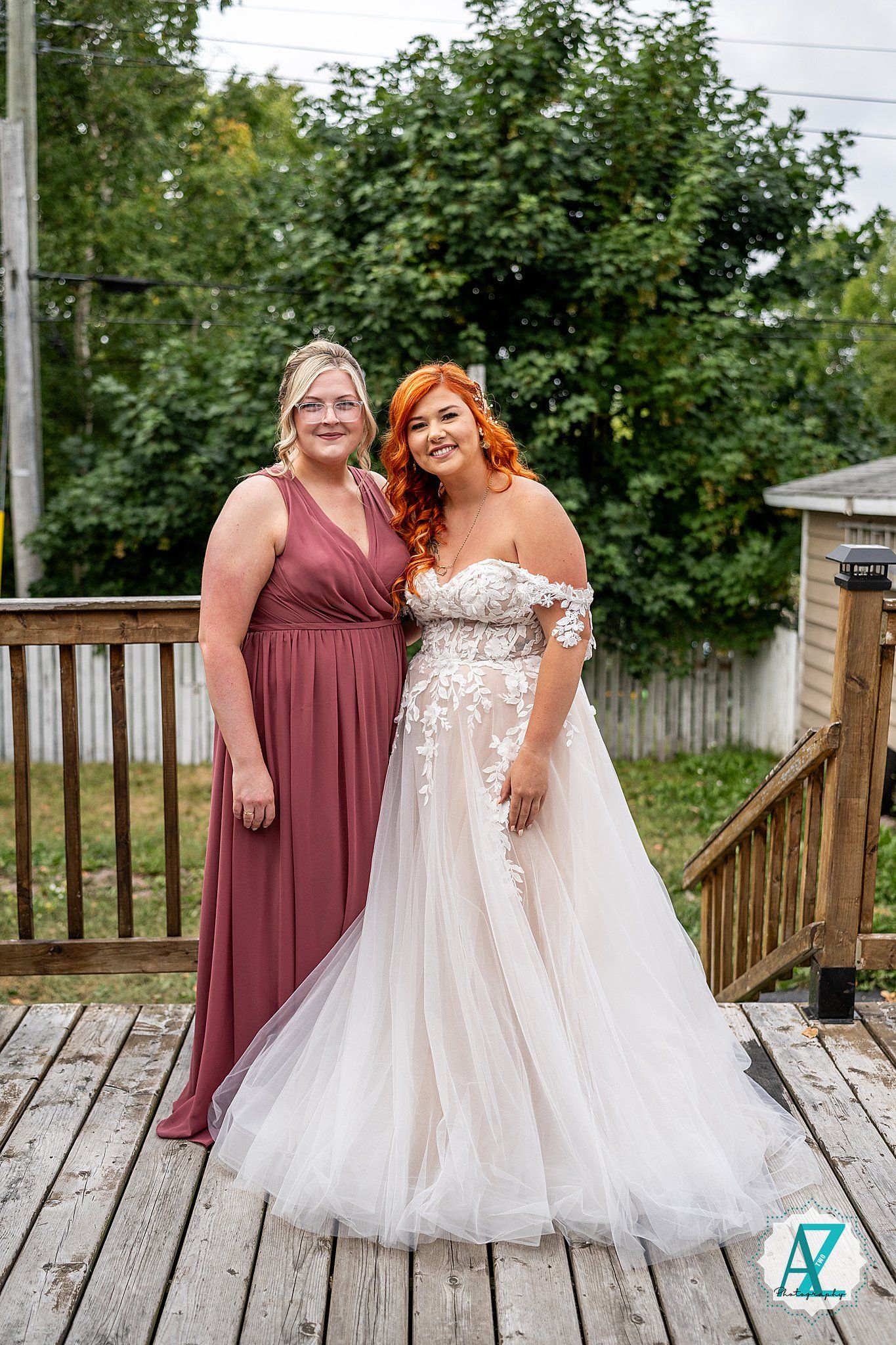 Wedding party members in burgundy and white dresses sharing happy moment on wooden deck.