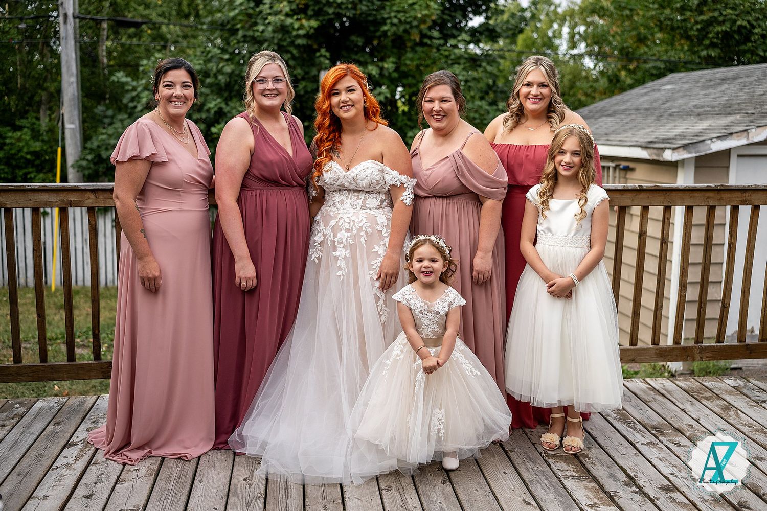 Bridesmaids in mauve dresses pose with flower girls in white tulle dresses.