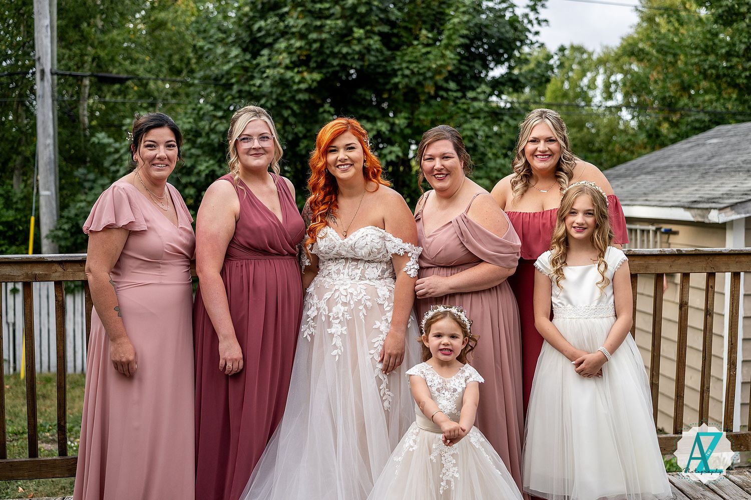 Wedding party in burgundy dresses posing on wooden deck for group photos.