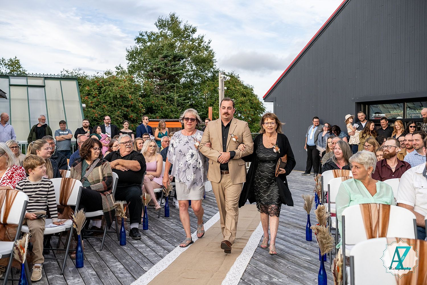 Large group of wedding guests mingle at an outdoor reception venue beneath a gray-toned sky.