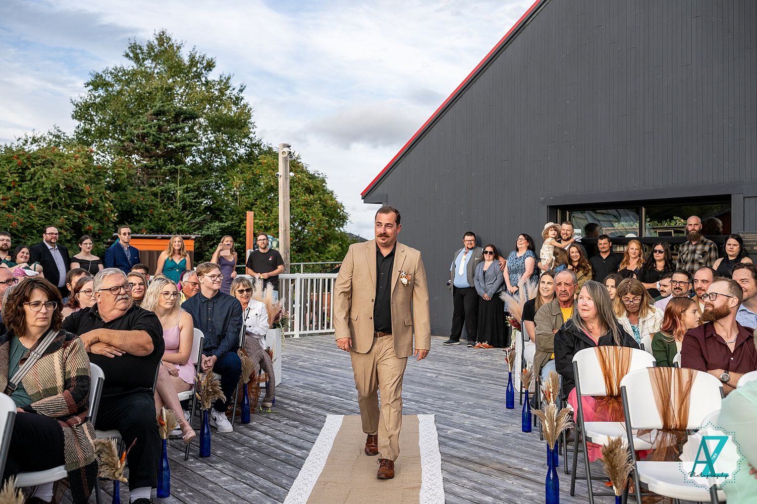 Wedding celebration on outdoor deck with guests lined up against grey building.