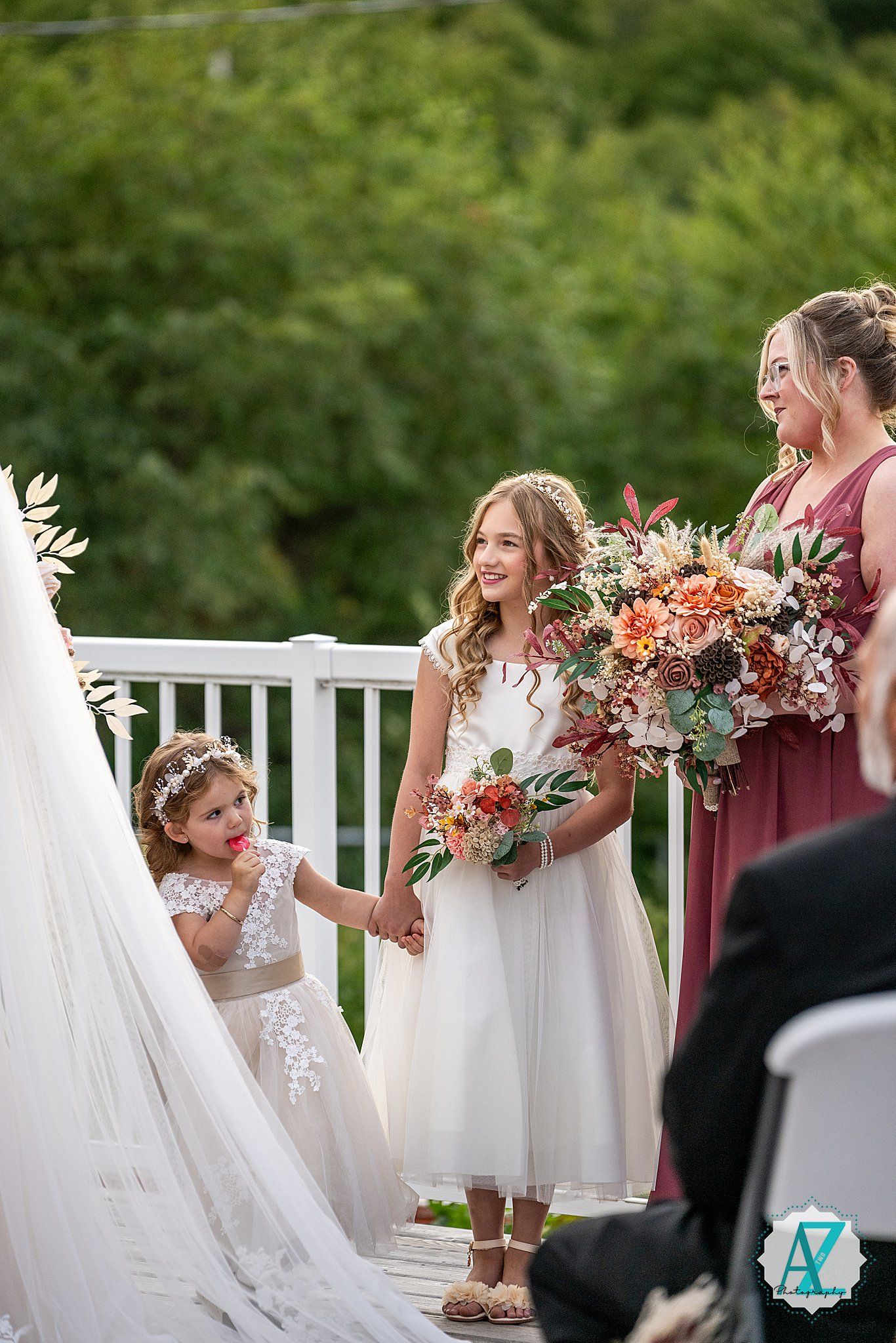 Wedding party holding coral-colored bouquets against lush green backdrop.