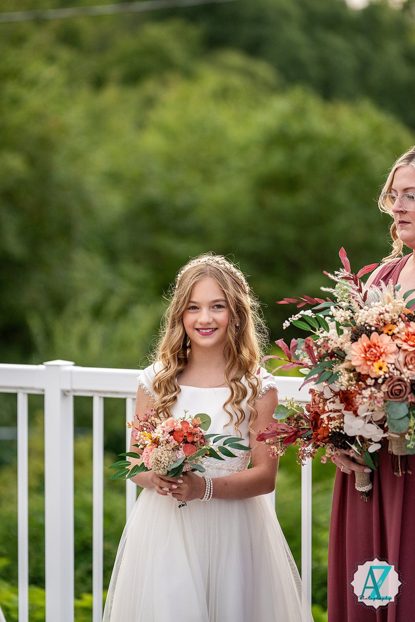 Bridesmaids in burgundy dresses hold peach and coral floral bouquets while smiling outdoors.