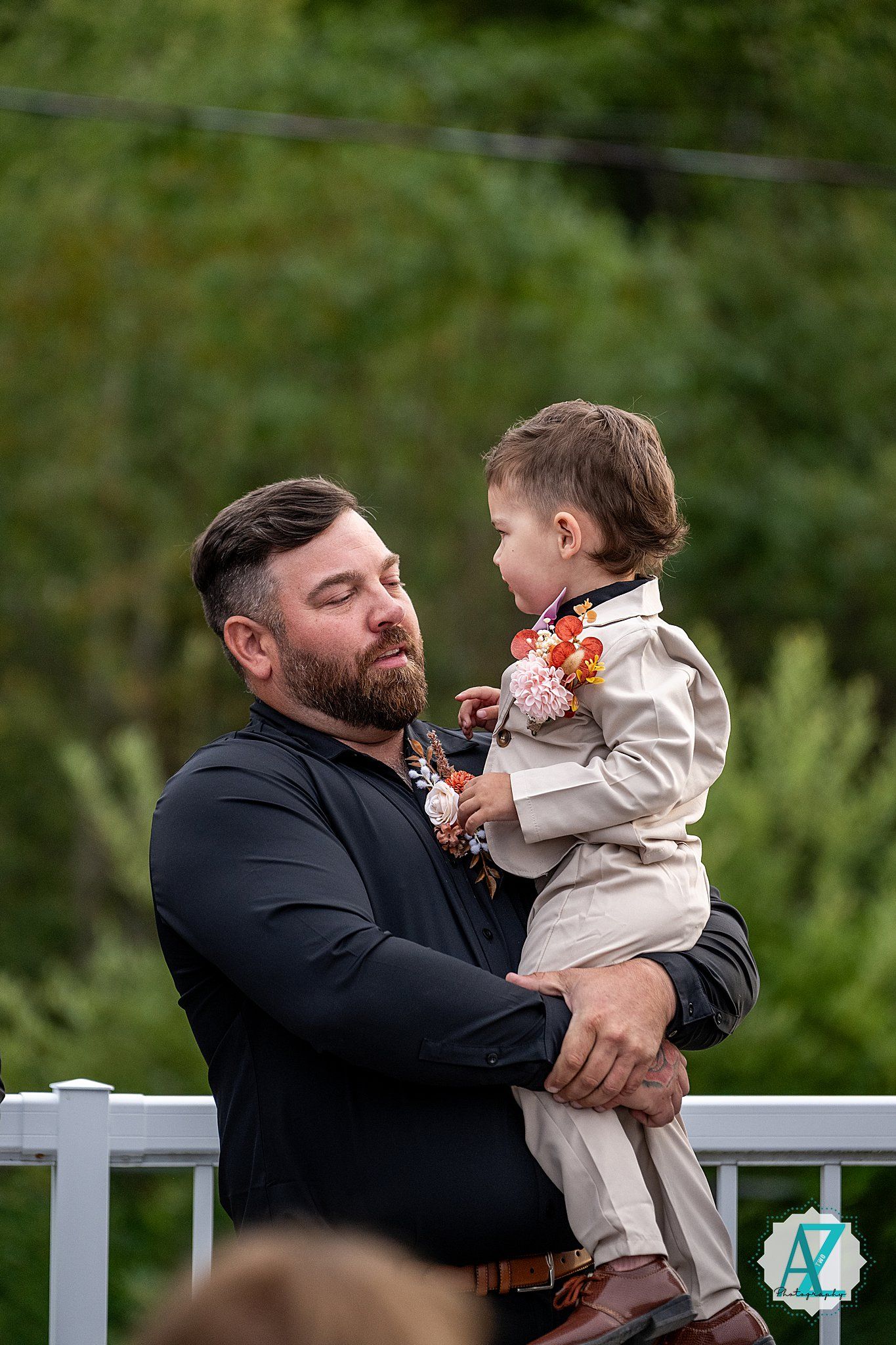 Emotional candid wedding moment on a white railing deck surrounded by greenery and flowers.
