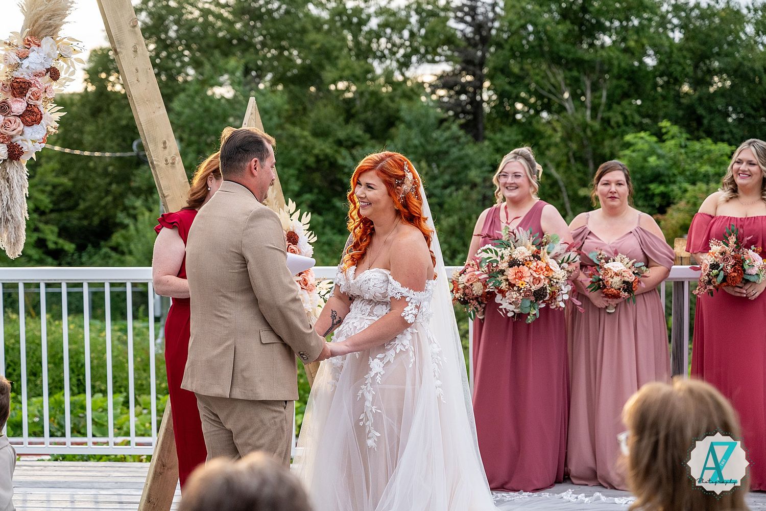 Outdoor wedding ceremony on a deck with pink floral decorations and scenic mountain views.