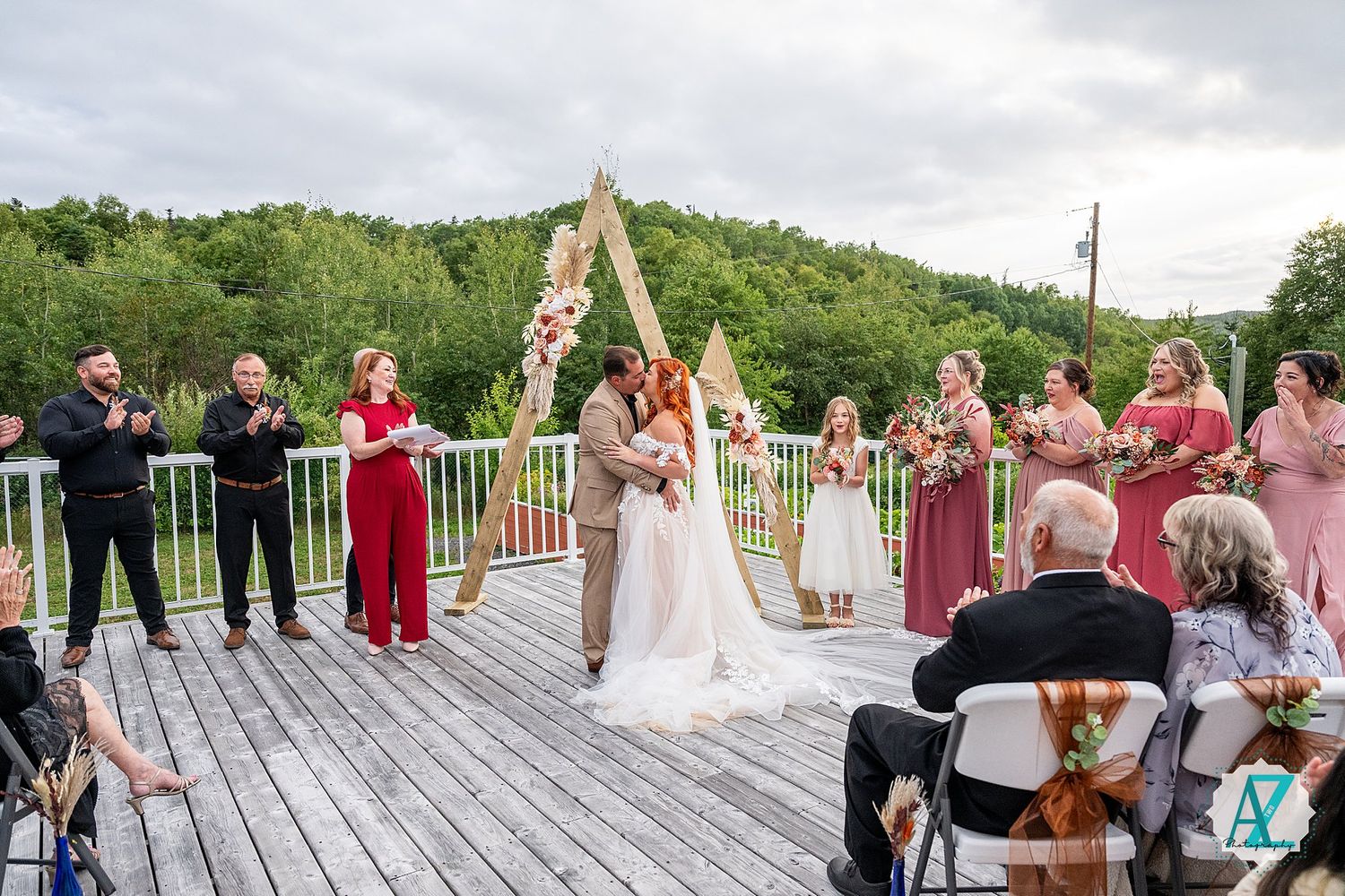 Outdoor wedding celebration with guests gathered on a wooden deck overlooking lush green mountains.