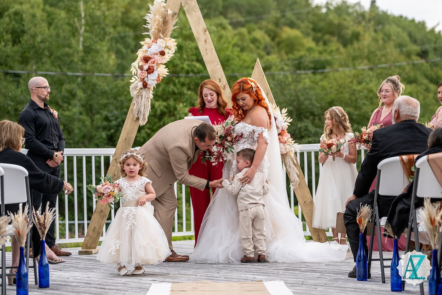 Outdoor wedding ceremony setup with wooden arch and white chairs on mountaintop deck.