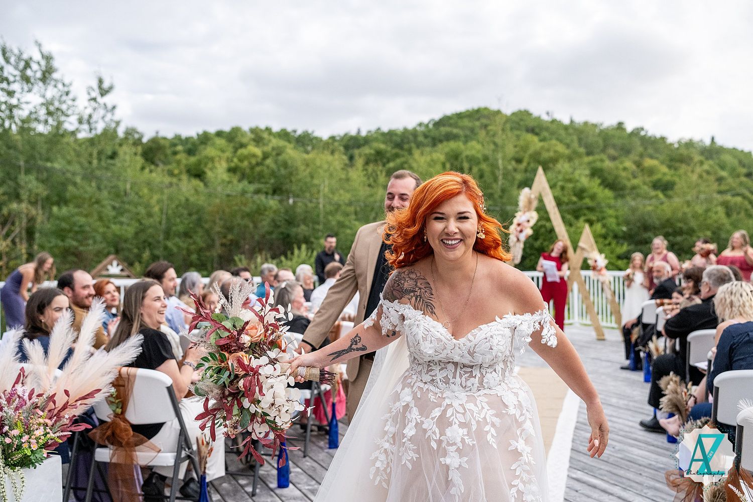 Joyful wedding celebration on an outdoor deck with mountains in the background and guests seated.