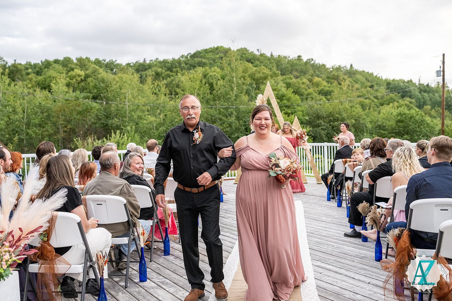 Wedding celebration on scenic deck with guests gathering in casual summer attire.