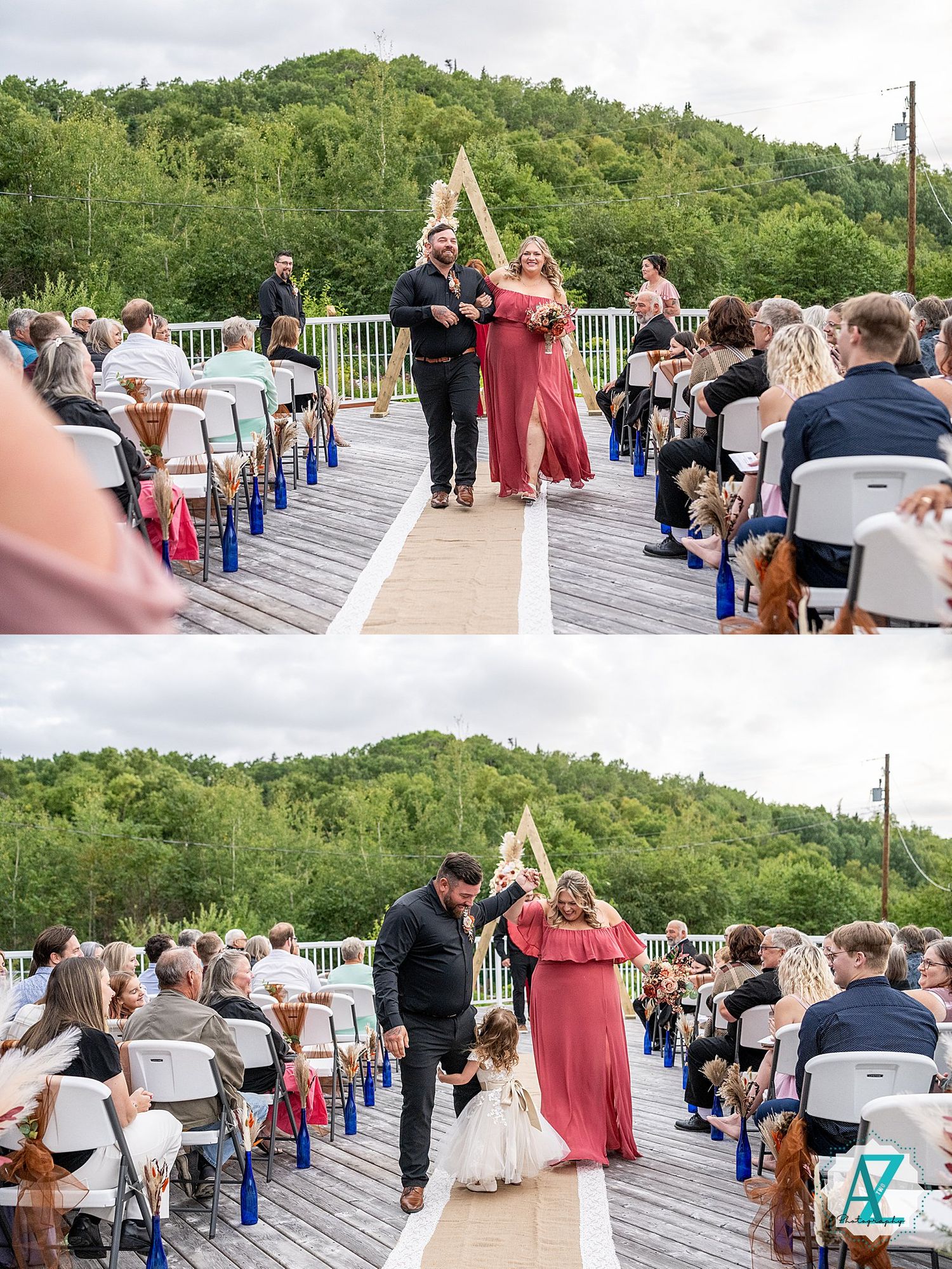 Wedding party members walk down outdoor deck aisle surrounded by white chairs and lush green mountain backdrop.