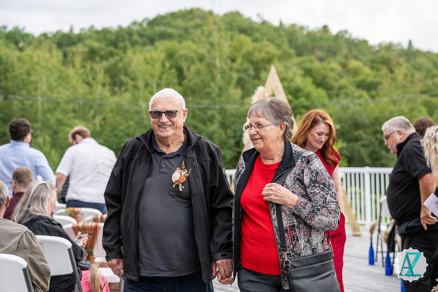 Wedding guests mingle and socialize on outdoor deck with mountain scenery.