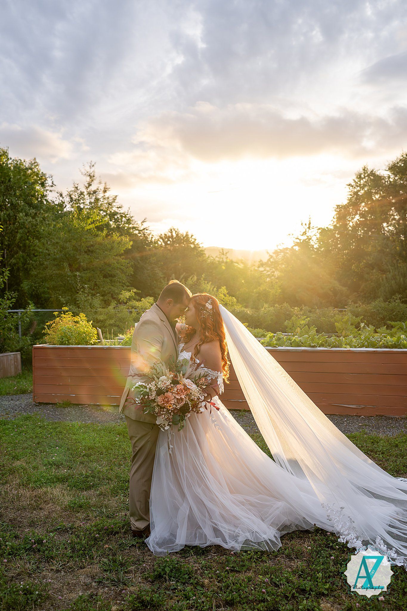 Romantic wedding couple shares intimate moment during golden hour sunset with flowing white dress and veil.
