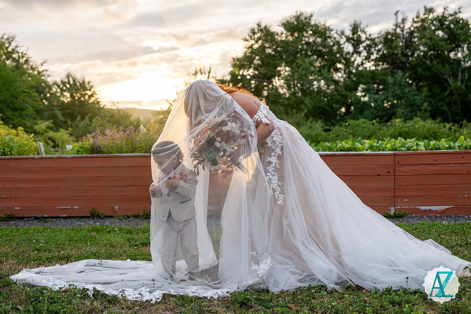 Wedding couple shares an intimate moment at sunset on a deck with a flowing white veil against a natural backdrop.