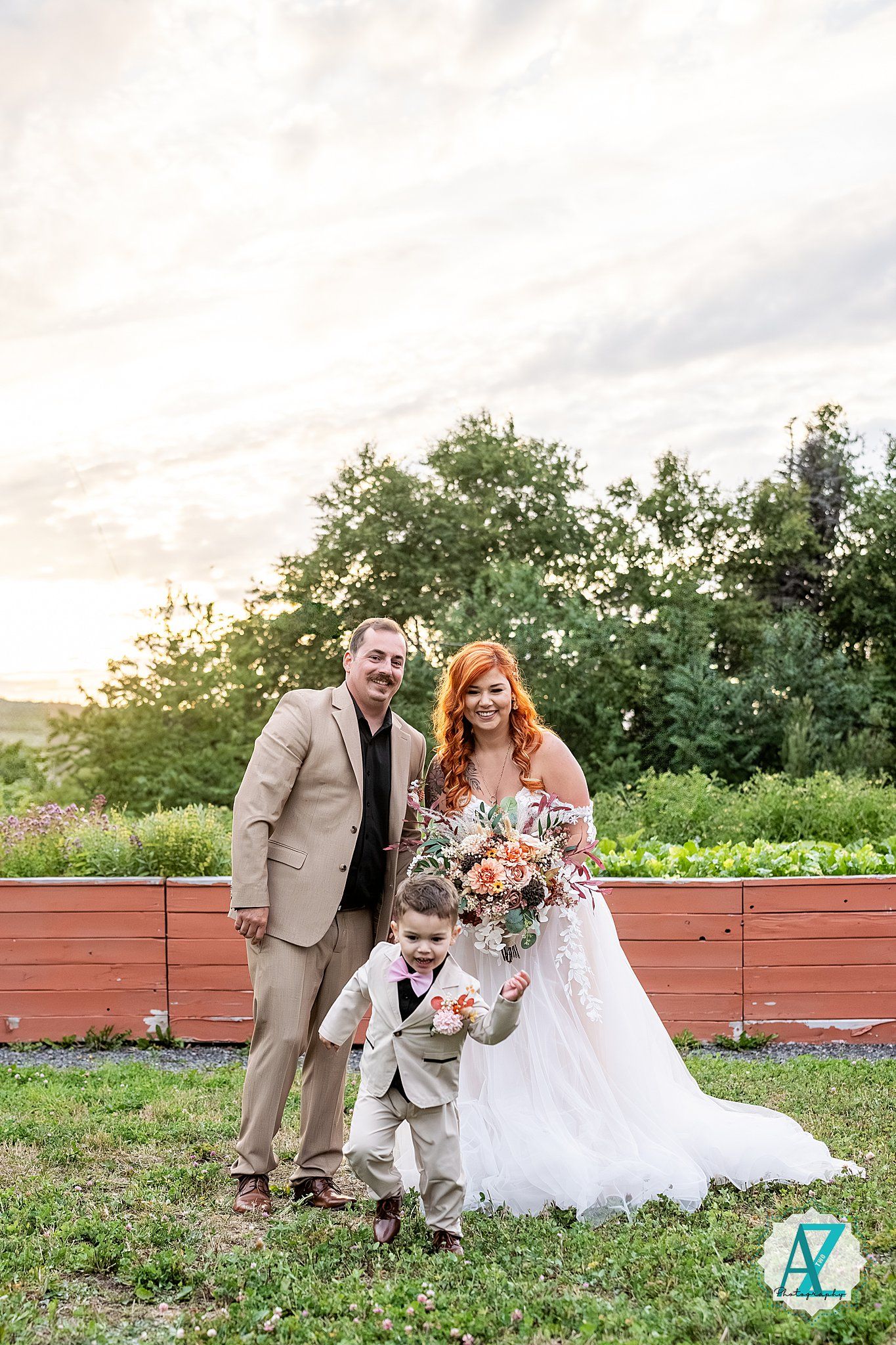 Wedding scene with couple and young attendant on outdoor deck against green summer landscape.