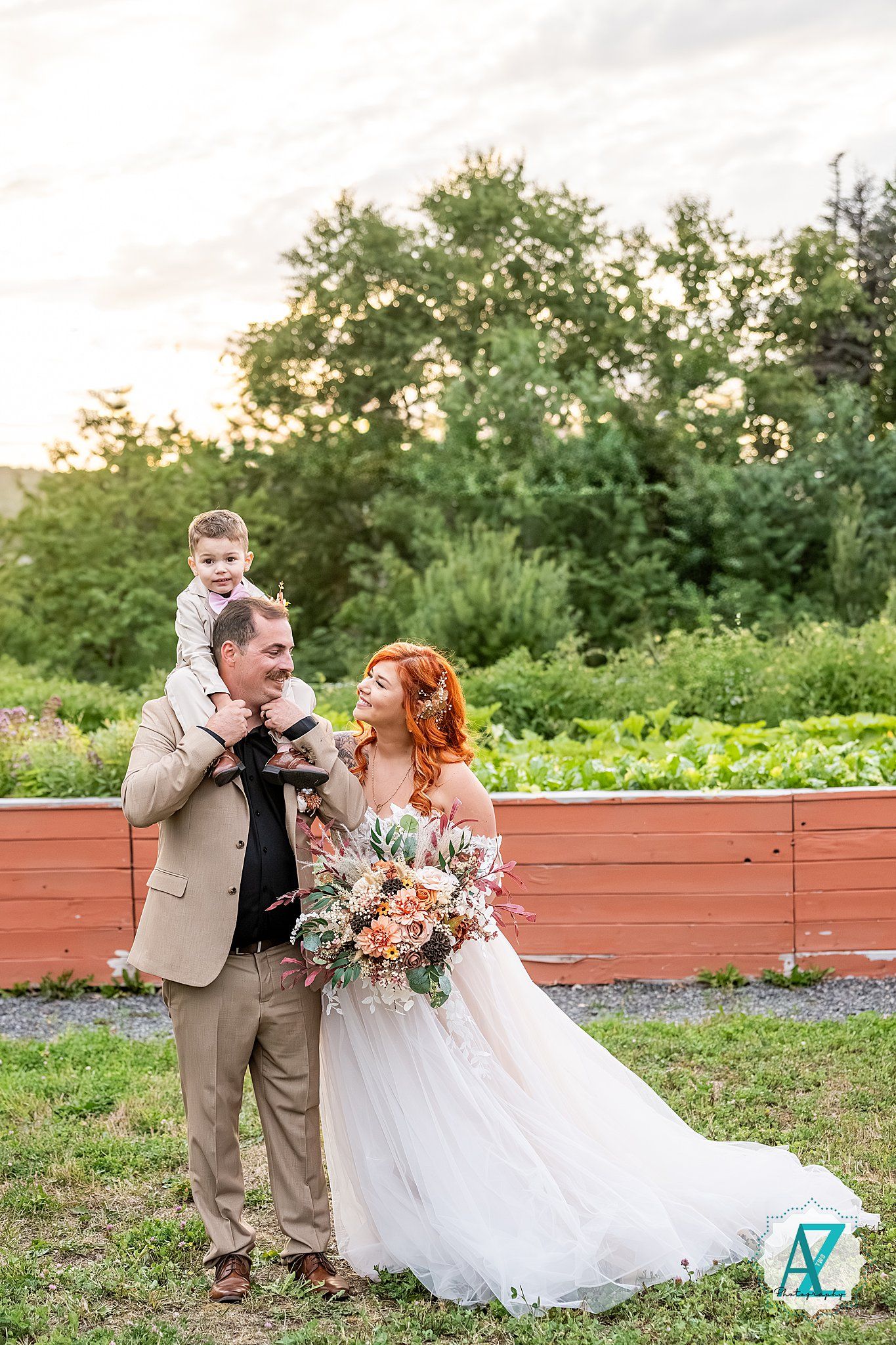 Romantic wedding couple poses with floral bouquet on rustic wooden deck at sunset.