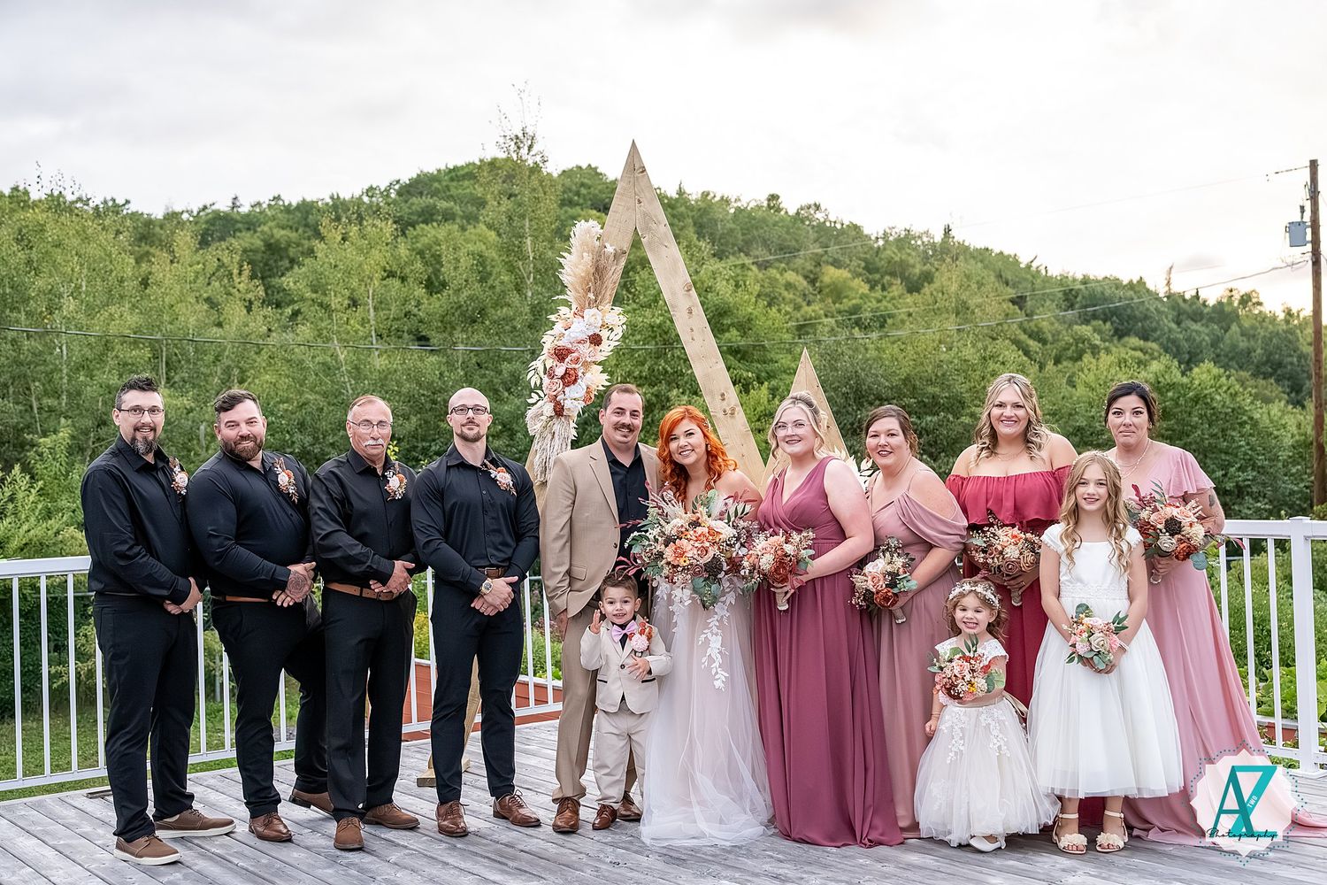 Wedding party members in mauve and tan colors gather on outdoor deck with scenic mountain view.