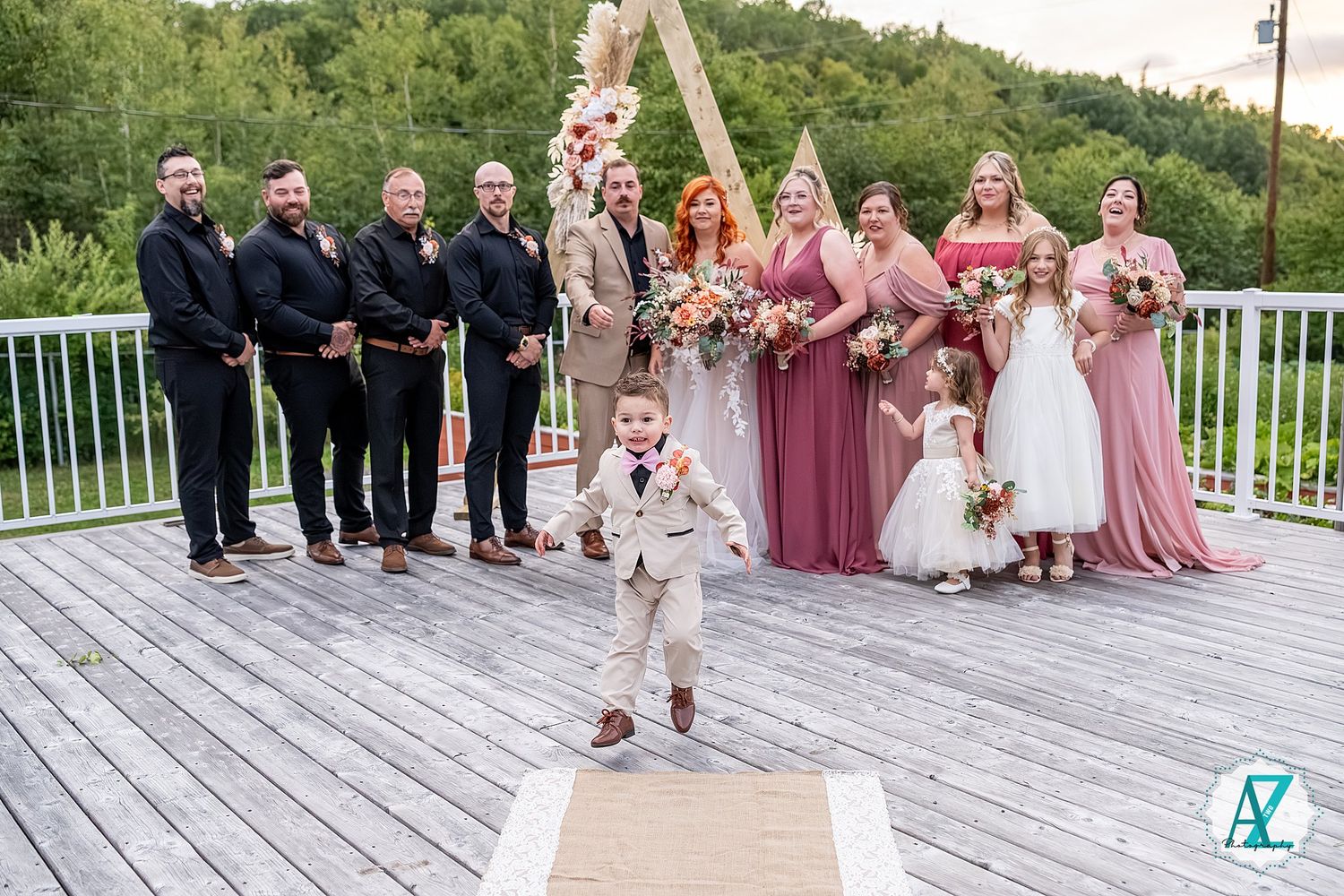 Large wedding party portrait on deck with mountains and geometric wooden arch backdrop.