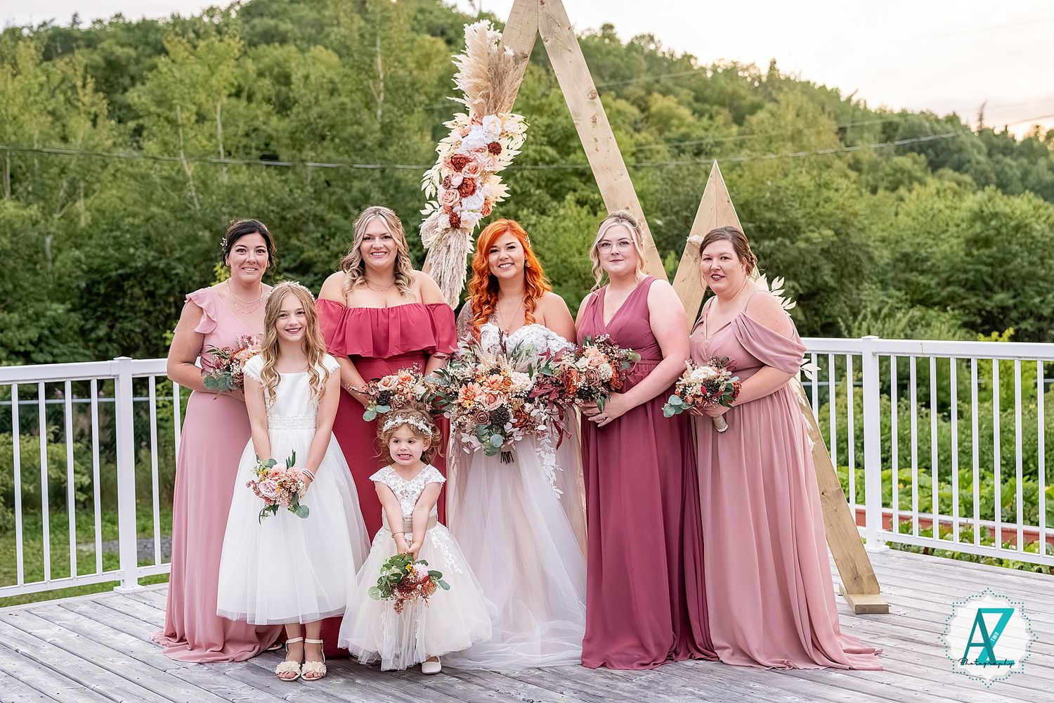 Wedding party in pink dresses poses on a deck overlooking green mountains.