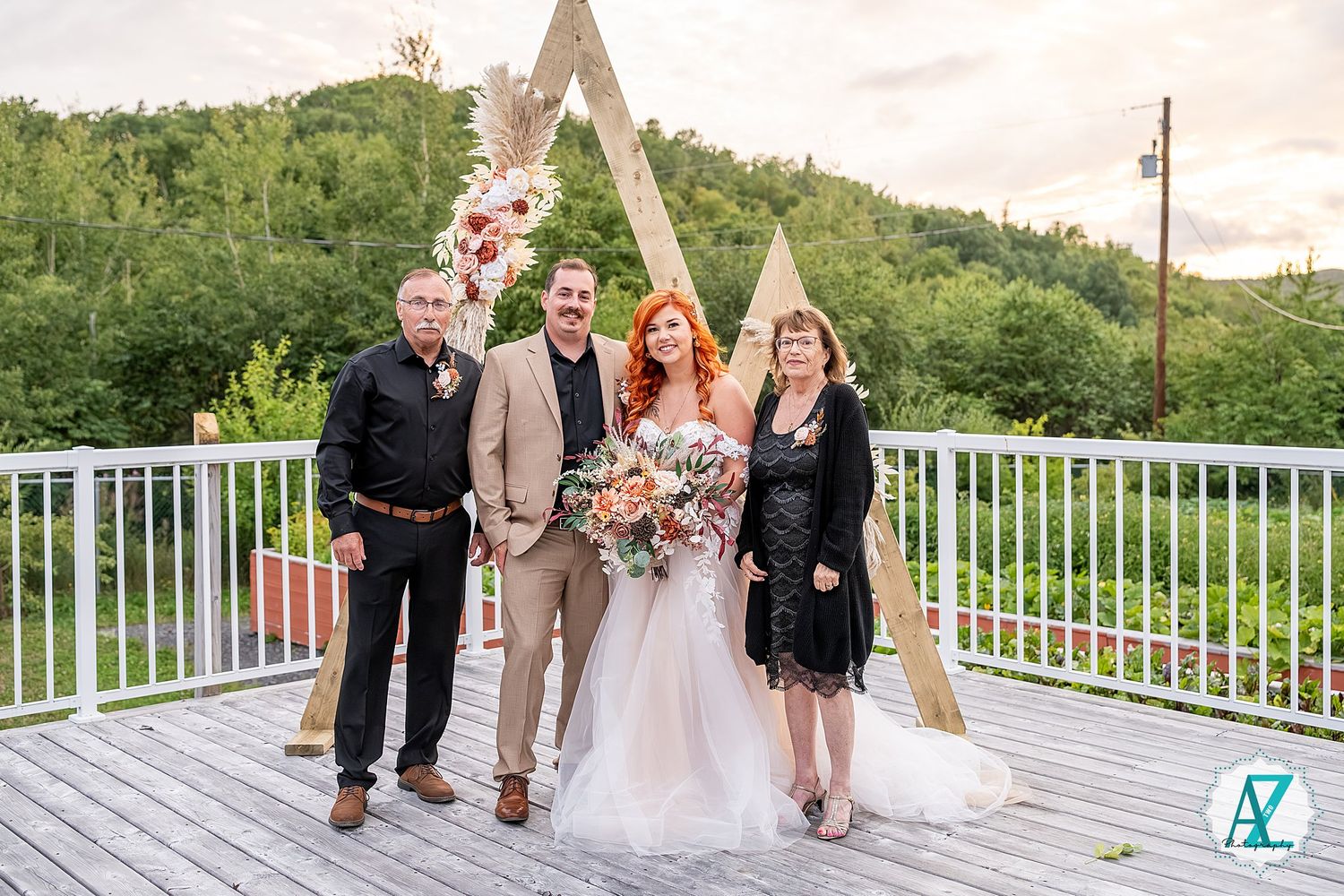 A group stands together in formal attire on a white deck railing overlooking a green landscape.