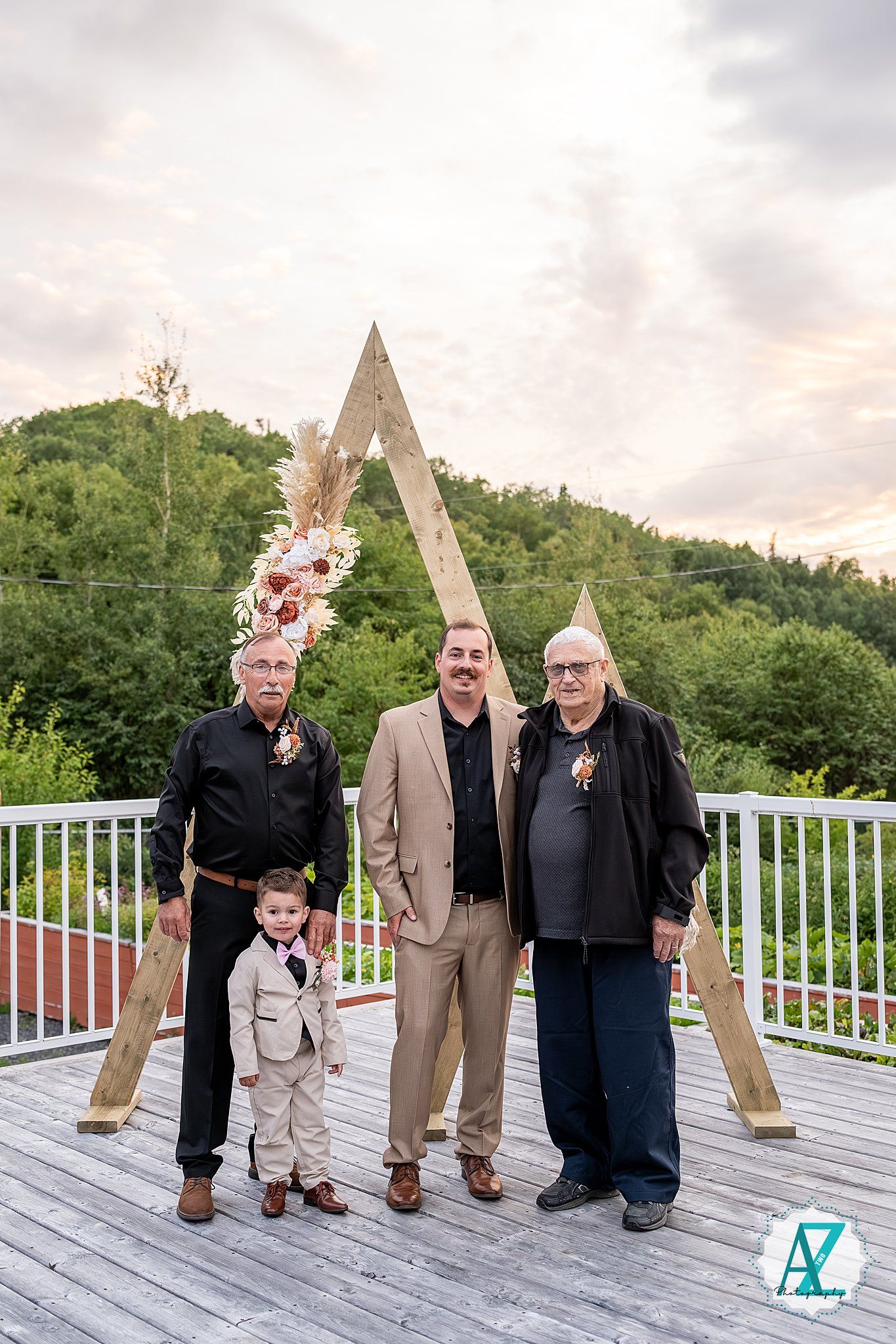 Family members gather for portrait on deck with decorated wooden arch and mountain views.