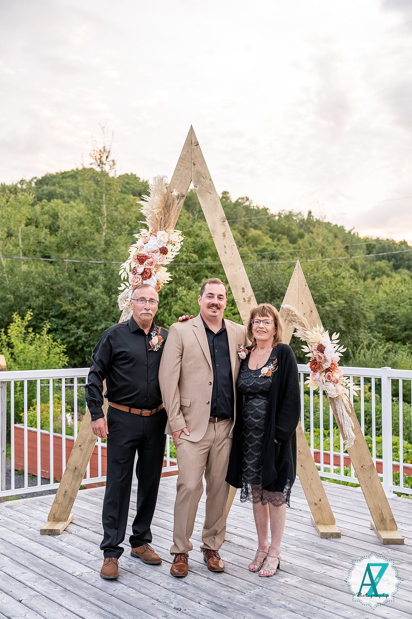 Small group poses together on outdoor deck with triangle wooden arch and summer greenery.