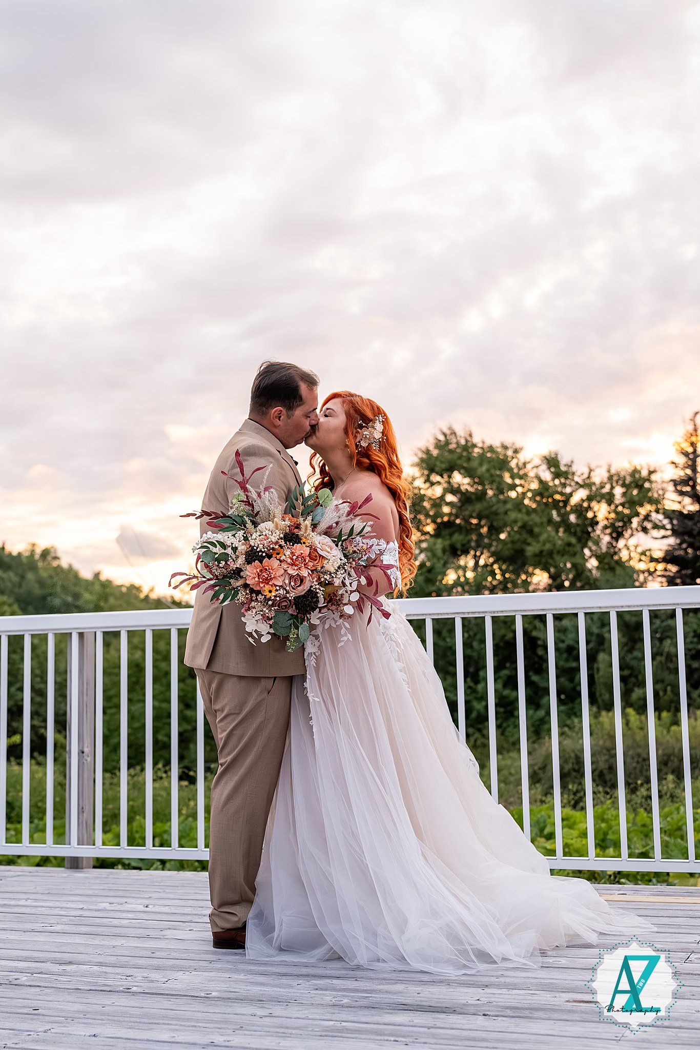 Intimate wedding moment captured on an outdoor deck with dramatic sunset clouds.
