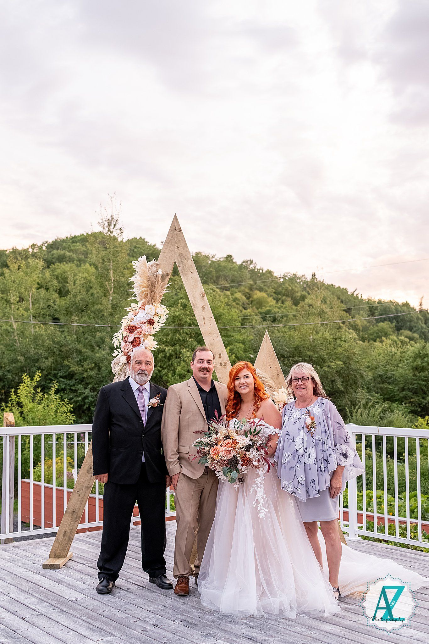 Wedding party gathered on a white deck overlooking a scenic mountain landscape.