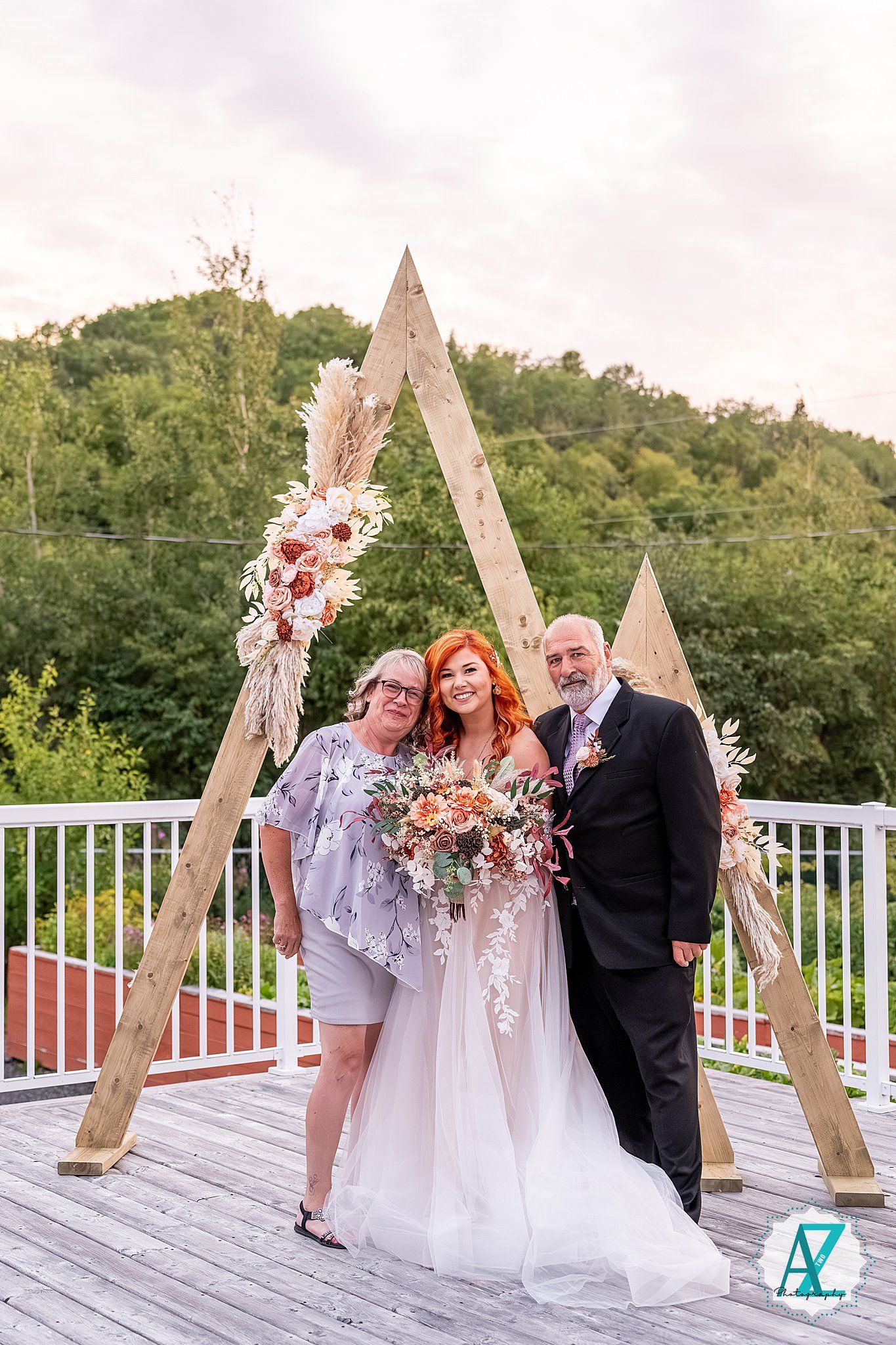 Wedding ceremony on outdoor deck with wooden triangle arch decorated in peachy floral arrangements.