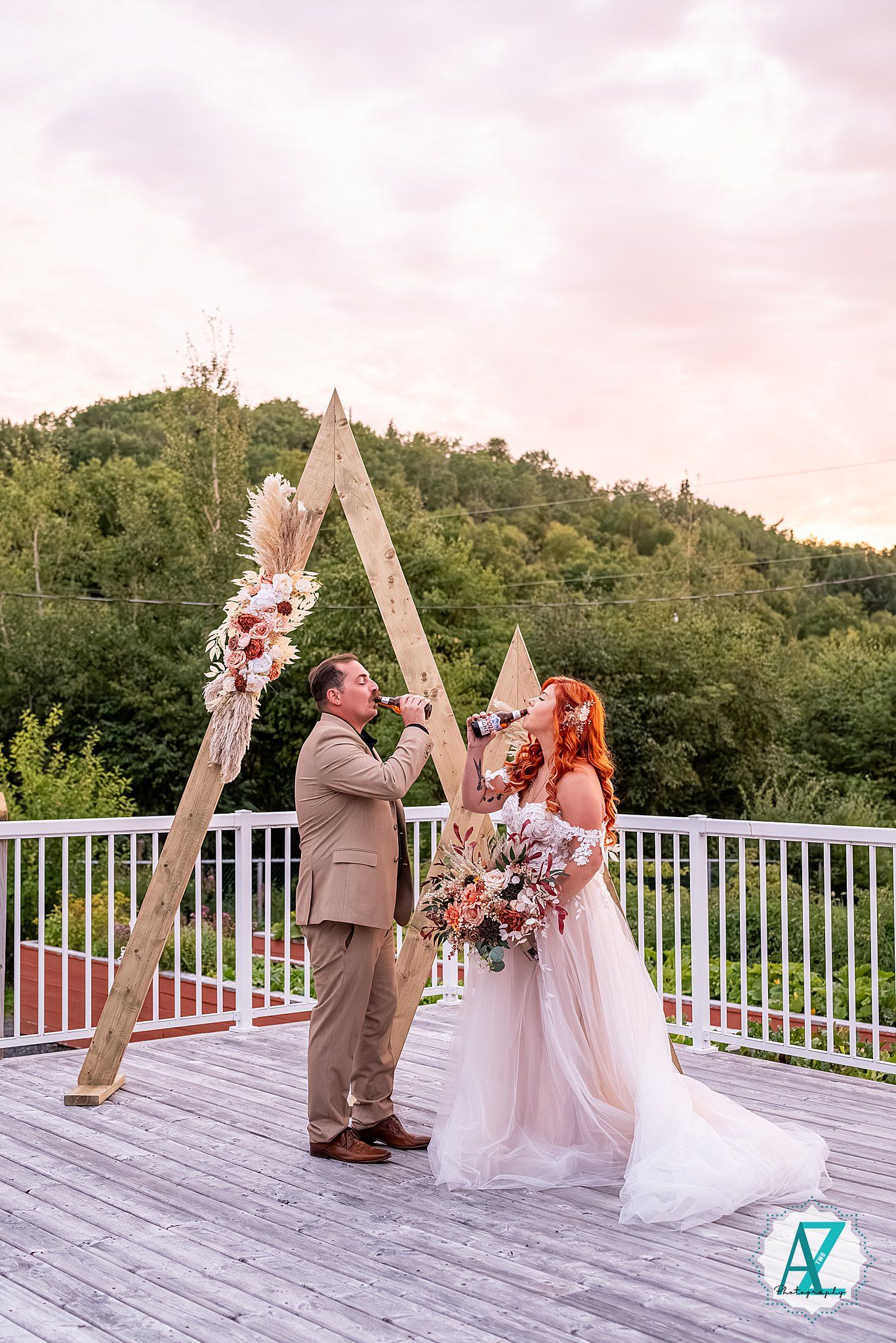 Wedding ceremony on a white deck with wooden triangle arches and sunset sky backdrop.