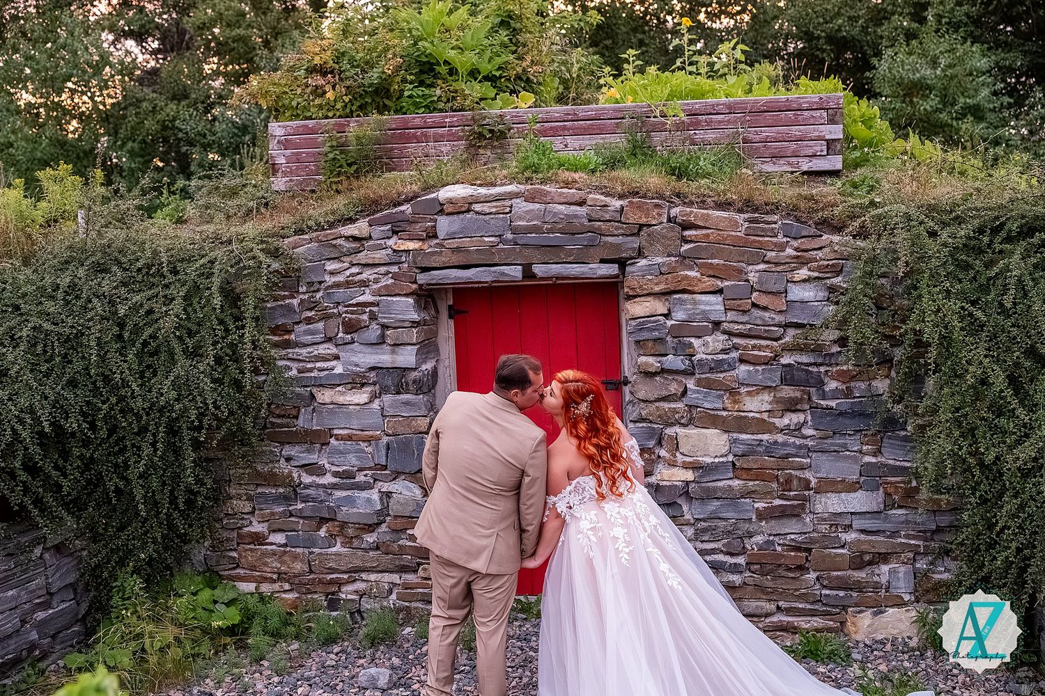 Wedding couple poses against rustic stone wall setting with vibrant red door.