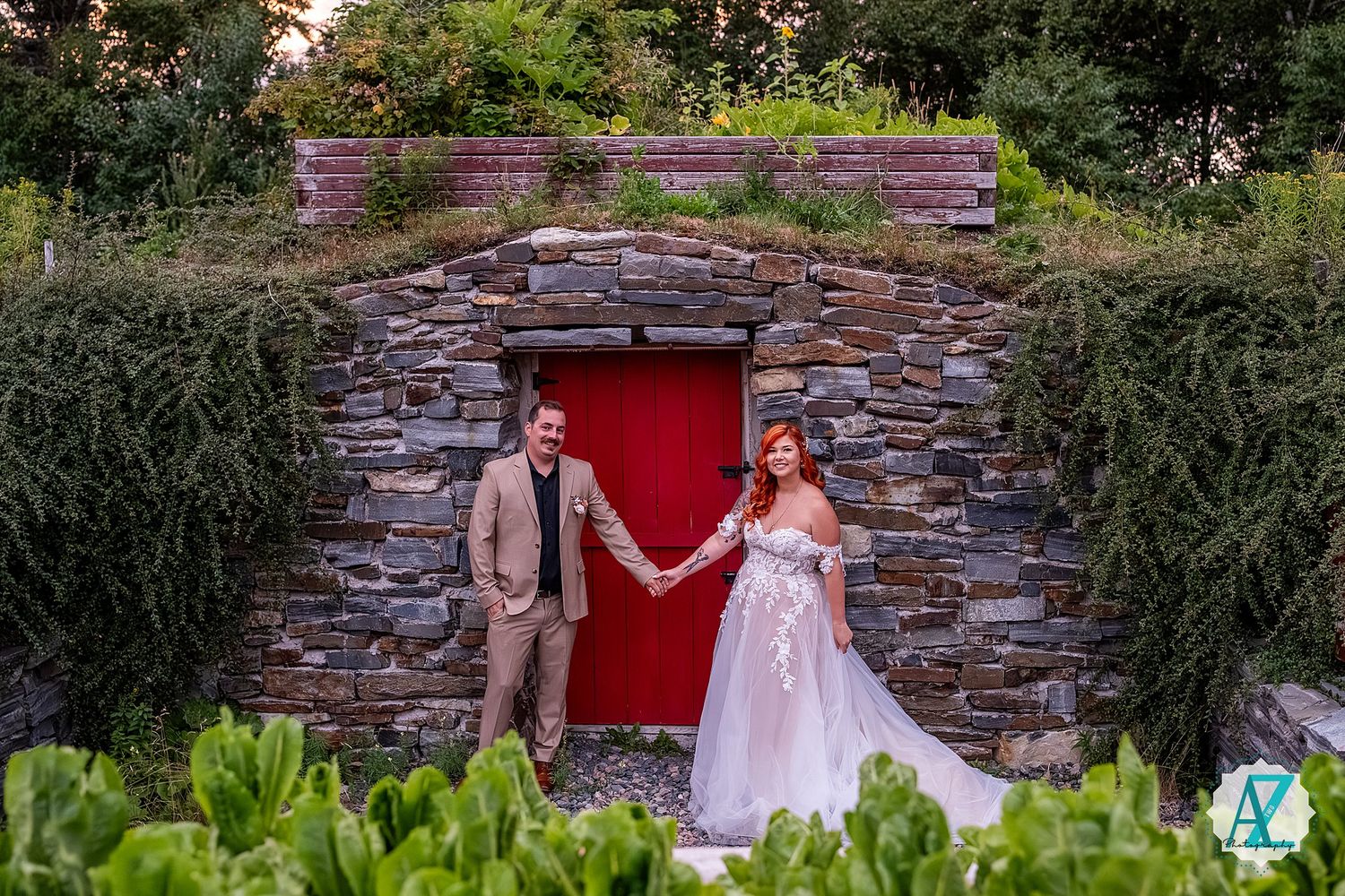 Newlyweds celebrating by a rustic stone wall with a bright red door in the garden backdrop.