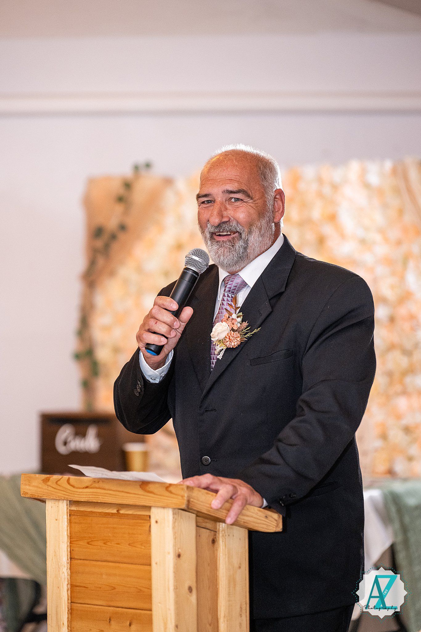 A speaker sits on a wooden podium giving a heartfelt speech during a wedding reception.
