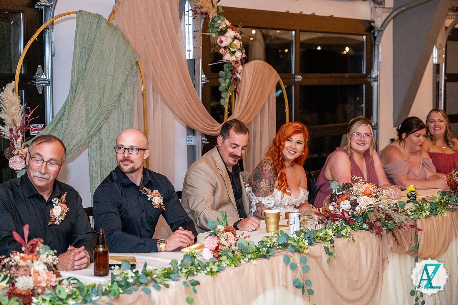 A formal dinner party with wedding guests seated at a long table decorated with lush floral centerpieces and candles.