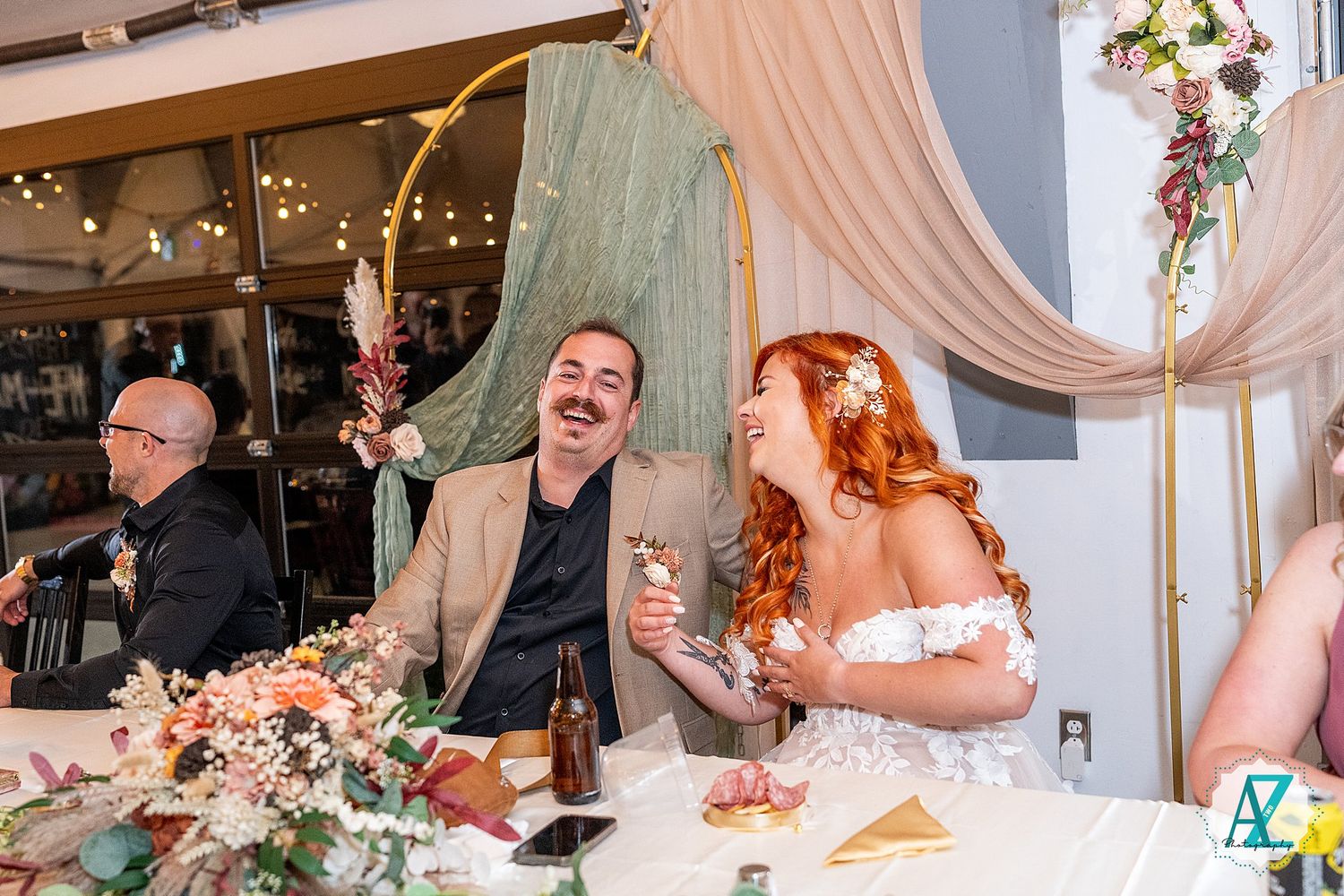 Festive wedding celebration shows guests enjoying themselves at decorated reception tables with string lights overhead.