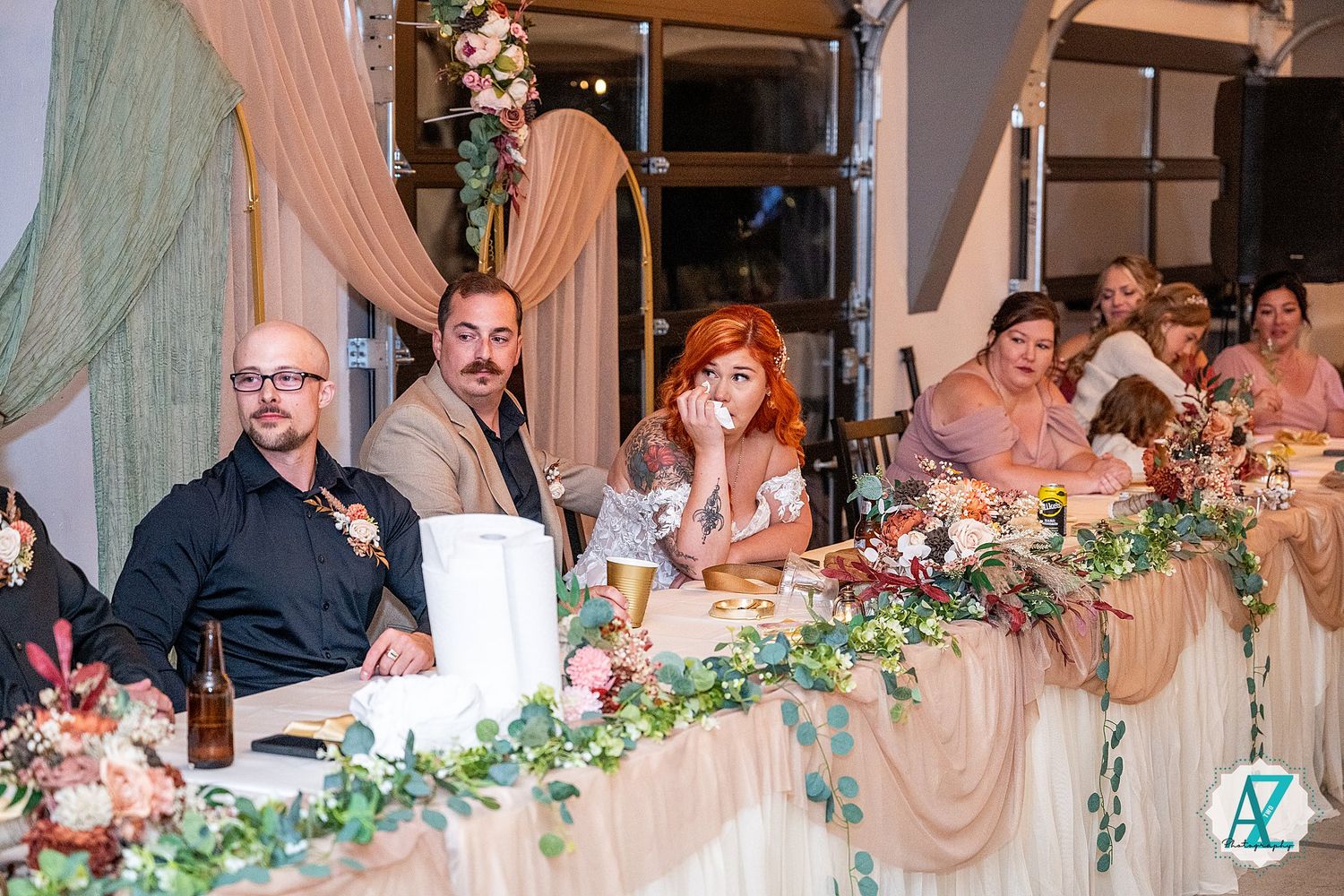 Wedding reception guests seated at decorated head table with floral garland.