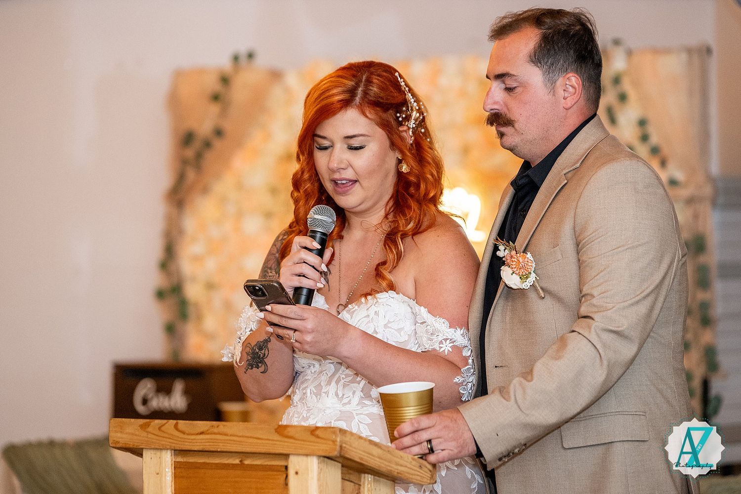 A couple gives toasts during their wedding reception against a light-colored backdrop with decor.