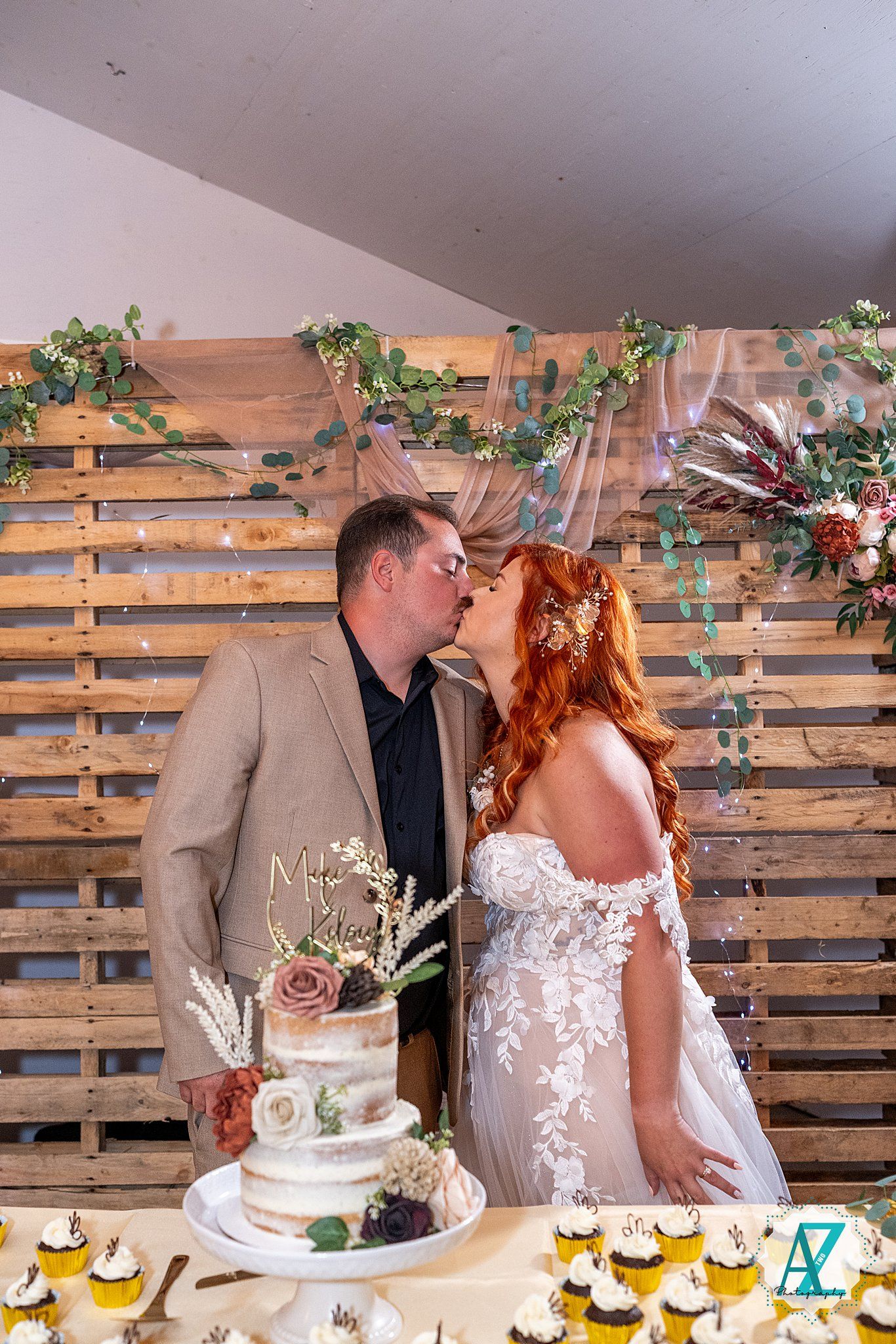 Wedding couple shares tender moment cutting cake together against rustic wooden pallet wall backdrop.