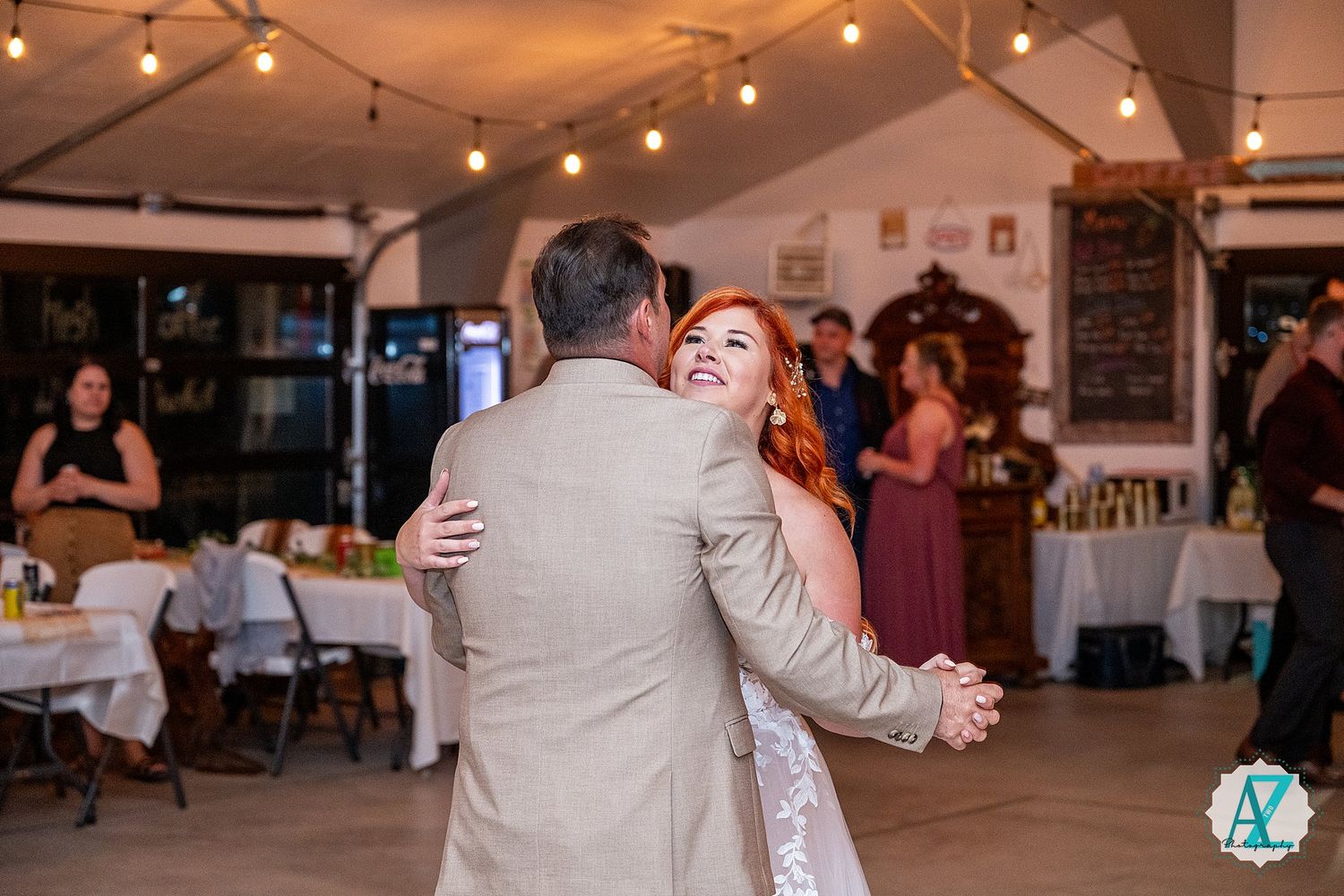 Wedding reception guests dancing under warm string lights at an indoor venue during evening celebration.