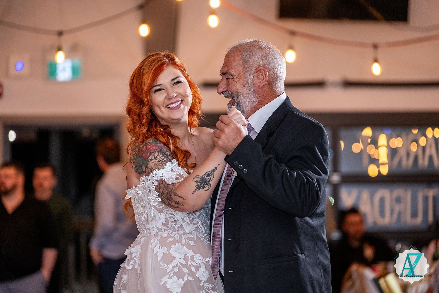 Two people share a joyful dance moment at a wedding celebration with string lights overhead.