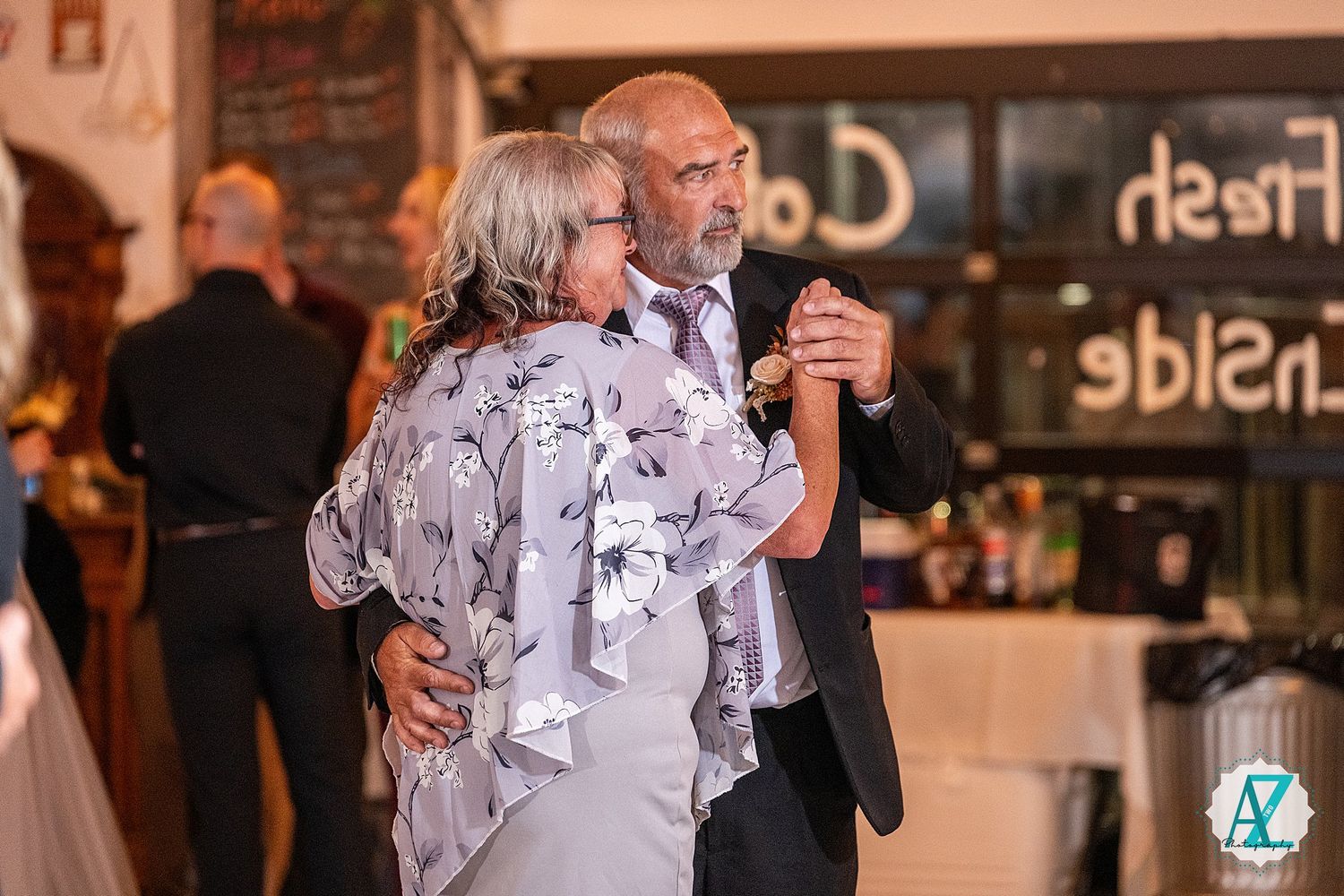 A couple dances together in an elegant reception hall decorated with warm lighting and rustic details.