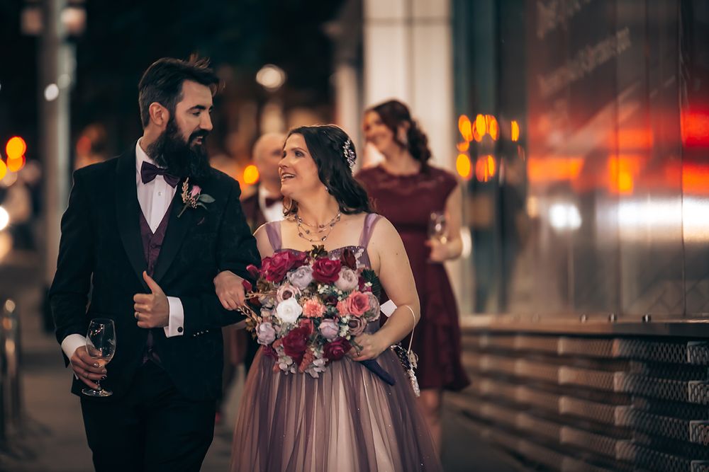 Wedding party in burgundy dresses and dark suits walk together during golden hour on an urban street.