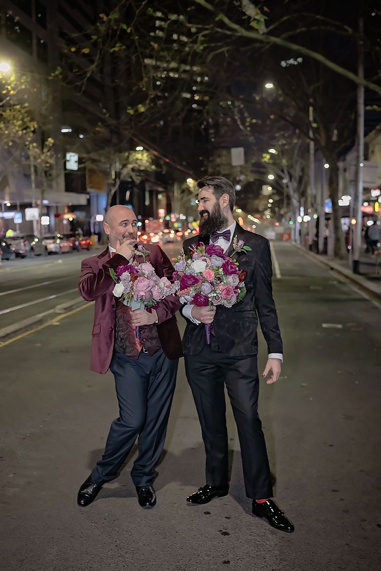 Three figures in formal attire walk together on a dimly lit city street at night.