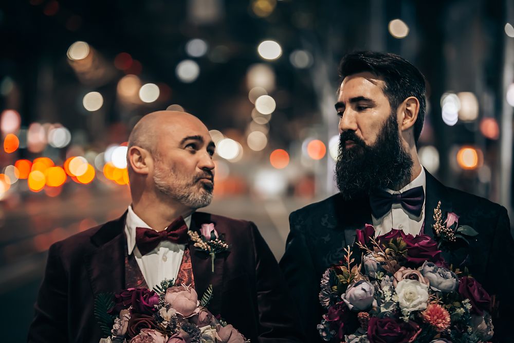 Romantic wedding party poses with vibrant floral bouquets against a dreamy bokeh background at dusk.
